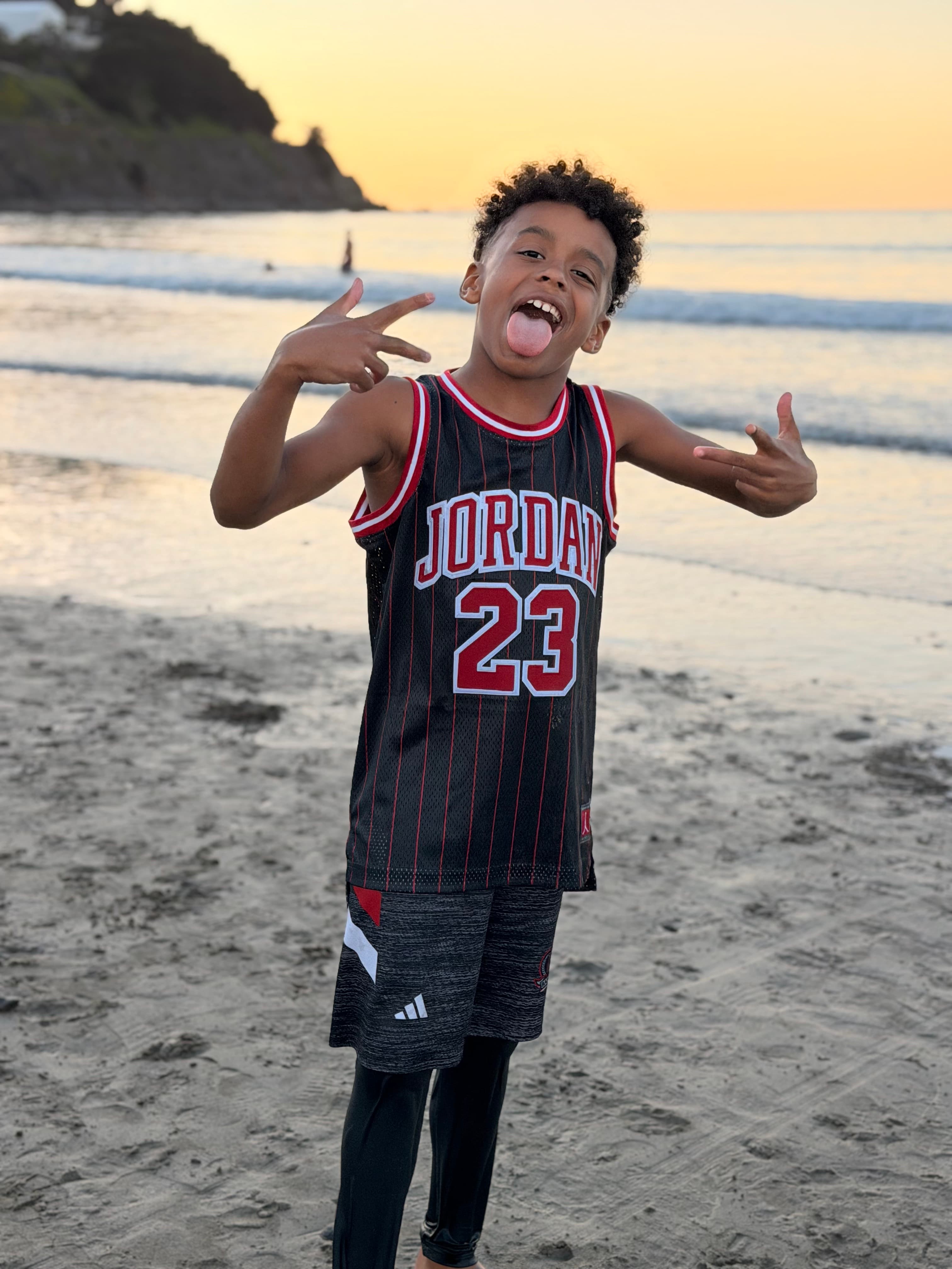 Jaiye in a number 23 jersey, throwing up a peace sign on the beach